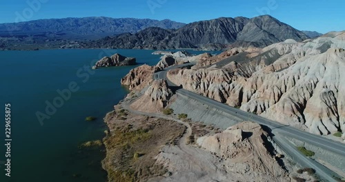Aerial drone scene flying over coast and road towards eroded white and orange sandstone mountains, blue lake at the side. Black and grey mountains at background. Cuesta del viento dam photo