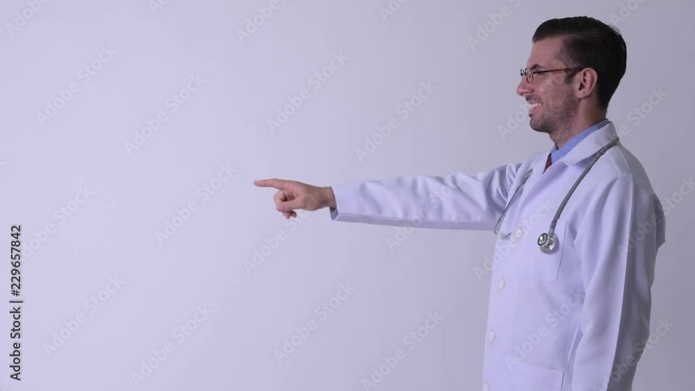 Profile view of young happy Hispanic man doctor pointing finger