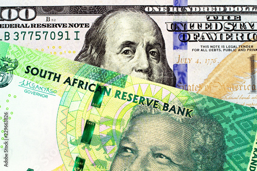 A close up image of a blue American one hundred dollar bill with a ten South African rand bank note