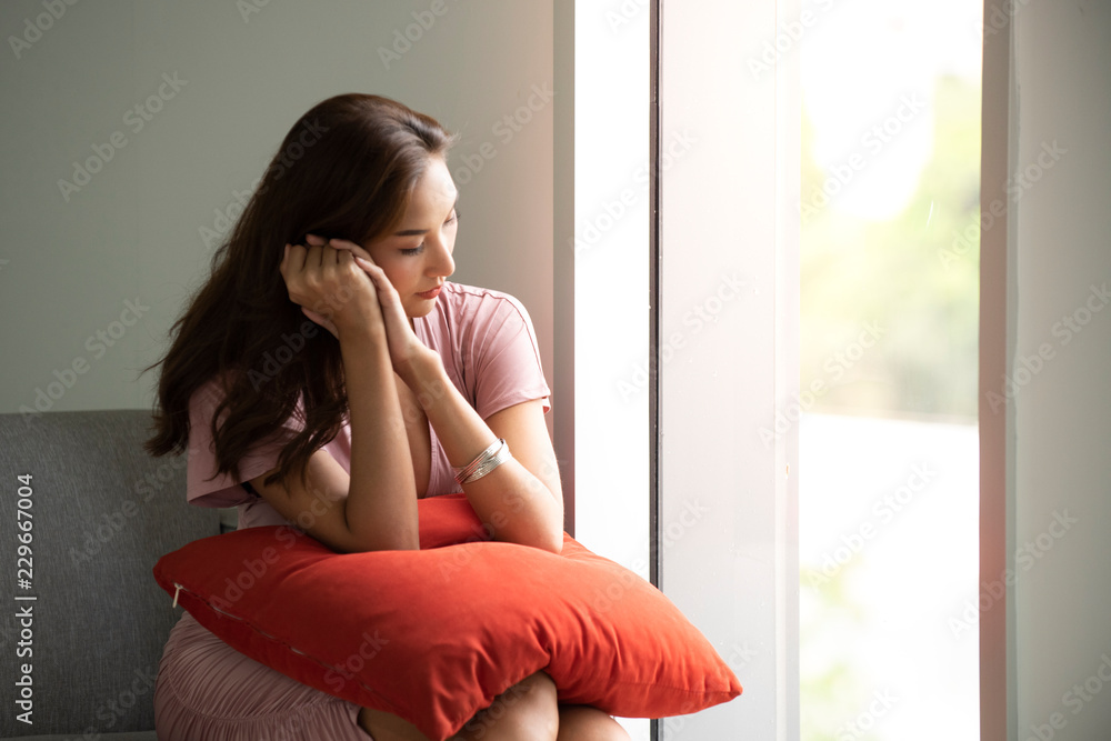 Young woman at home sitting on modern chair in front of window relaxing in her living room Young woman at home sitting on modern chair in front of window relaxing in her living room