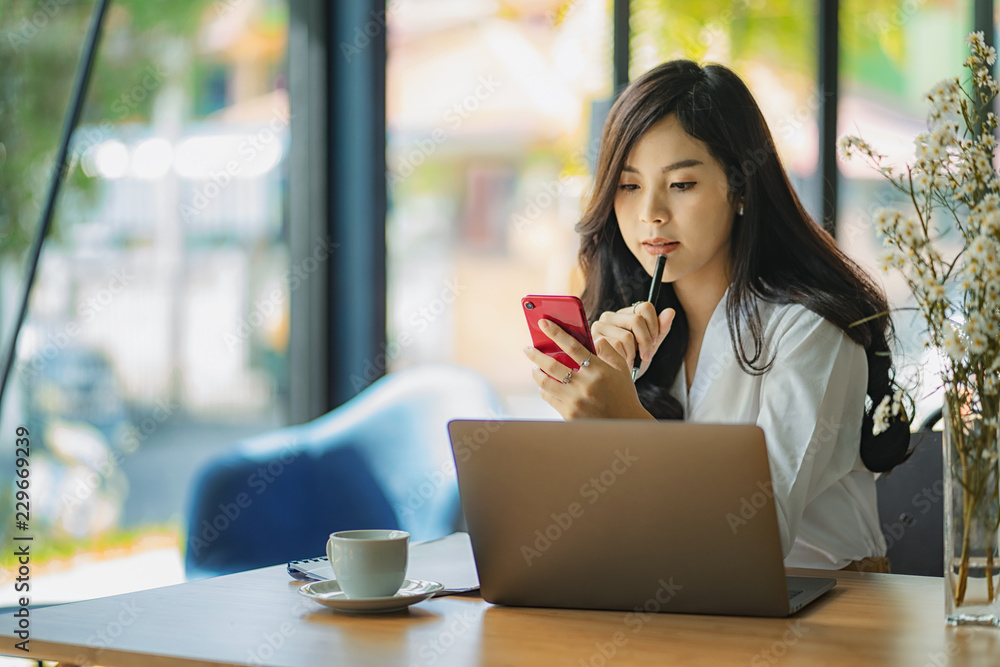 Young Asian female entrepreneur talking on the phone while working at home office. Young Asian female entrepreneur talking on the phone while working at home office.