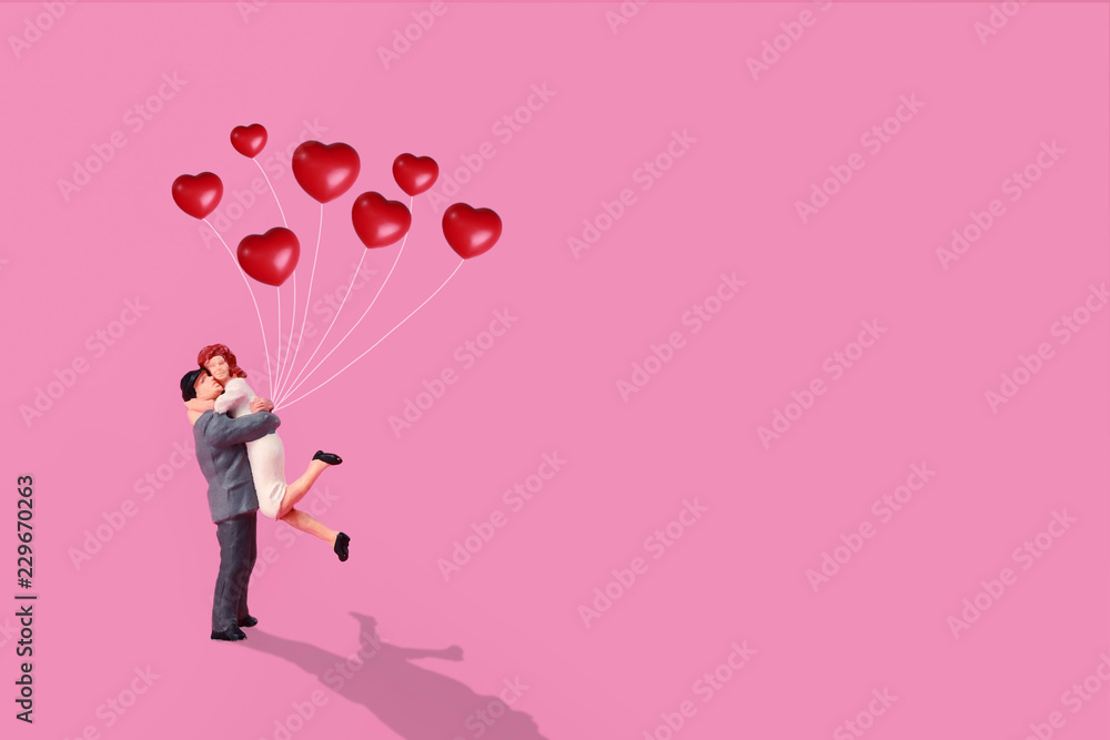 miniature couple standing and holding red love balloon in pink background miniature couple standing and holding red love balloon in pink background