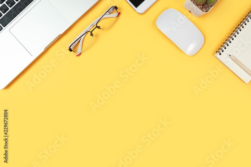 workspace table with laptop computer, office supplies, coffee cup, cell phone and coffee cup on yellow background