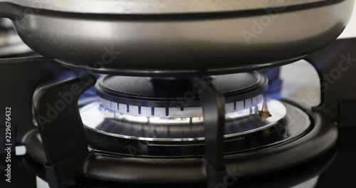 Hand turning on gas stove with frying pan