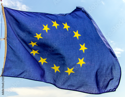 Flag of the European Union flutters on the blue sky. A blue flag with yellow stars in circles - the EU symbol winds in the wind.