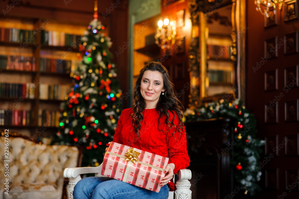 Beautiful girl in a red sweater near the Christmas tree.