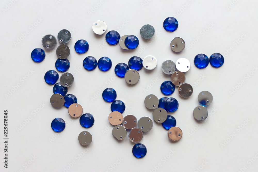 A handful of shiny blue sequins for needlework, lying on the light surface of the table. Top view A handful of shiny blue sequins for needlework, lying on the light surface of the table. Top view