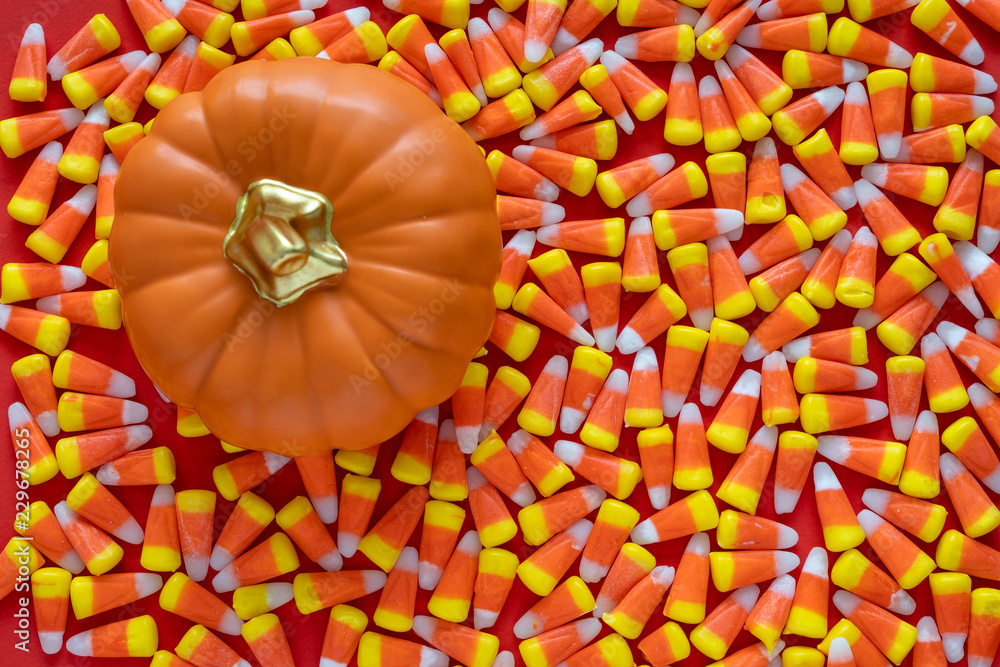Fototapeta premium Big pile of Halloween candy corn on an orange background, with a ceramic orange pumpkin 