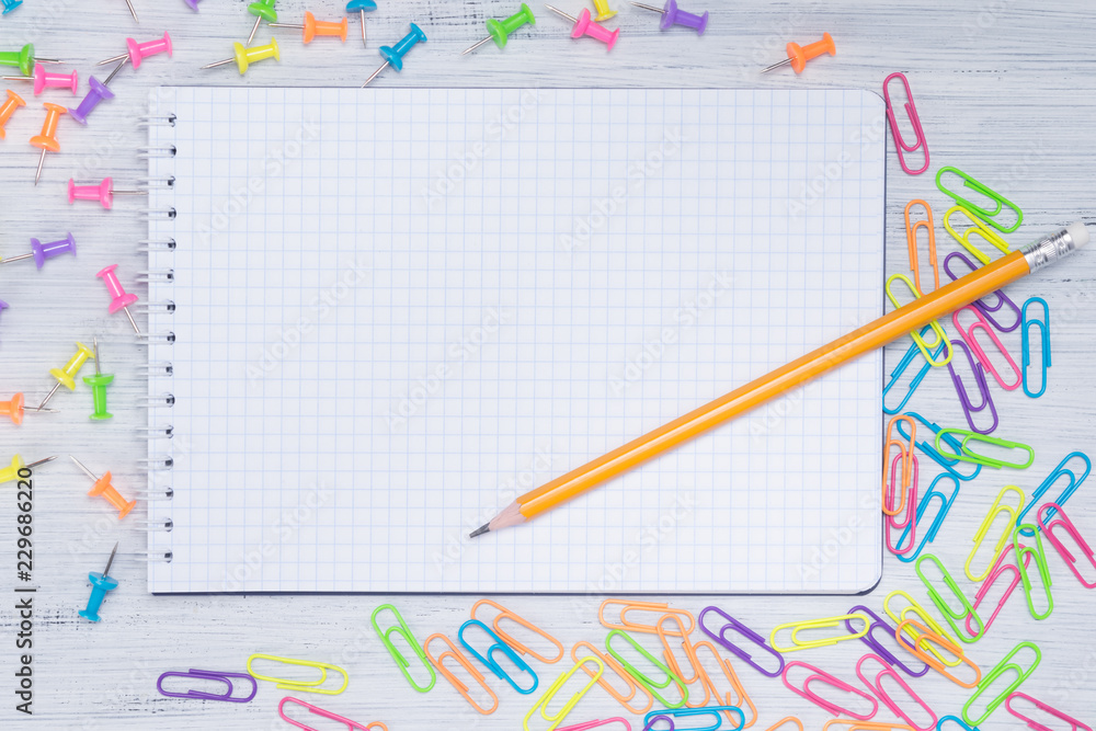 a blank piece of paper in a cage, on the table with a pencil surrounded by multi-colored clips a blank piece of paper in a cage, on the table with a pencil surrounded by multi-colored clips