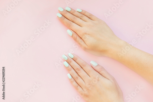 Tender hands with perfect blue manicure on trendy pastel pink background. Place for tex