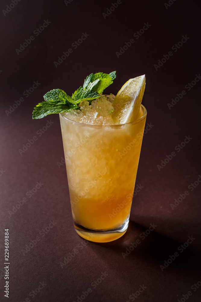 Glass of orange cocktail with mint, ice and slice of orange on elegant dark brown background Glass of orange cocktail with mint, ice and slice of orange on elegant dark brown background