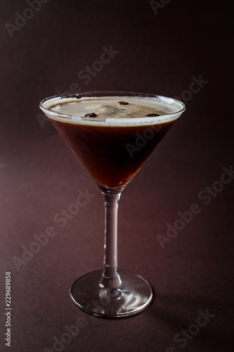 Glass of espresso martini with coffee beans and vodka on elegant dark brown background