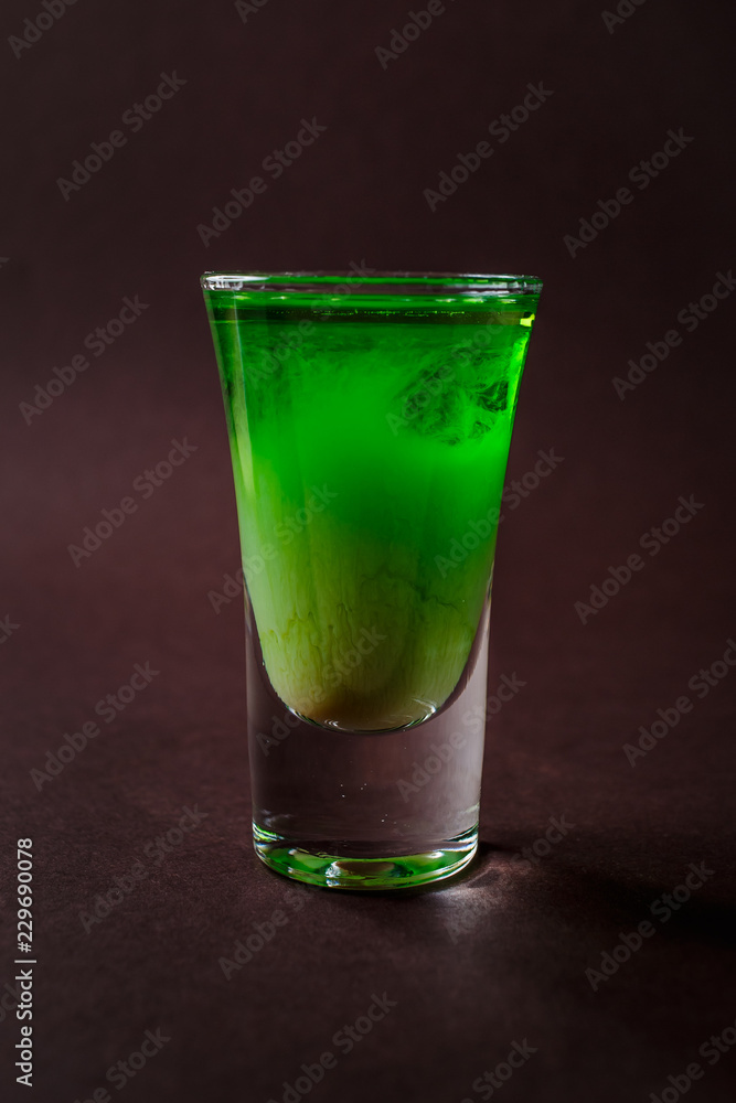Green alcoholic shot glass with absent, irish cream, liquor on elegant dark brown background Green alcoholic shot glass with absent, irish cream, liquor on elegant dark brown background