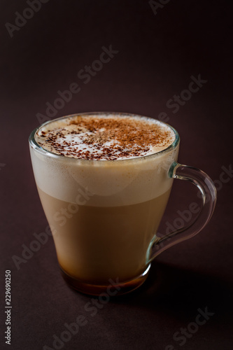 Glass of coffee with chocolate topping on elegant dark brown background
