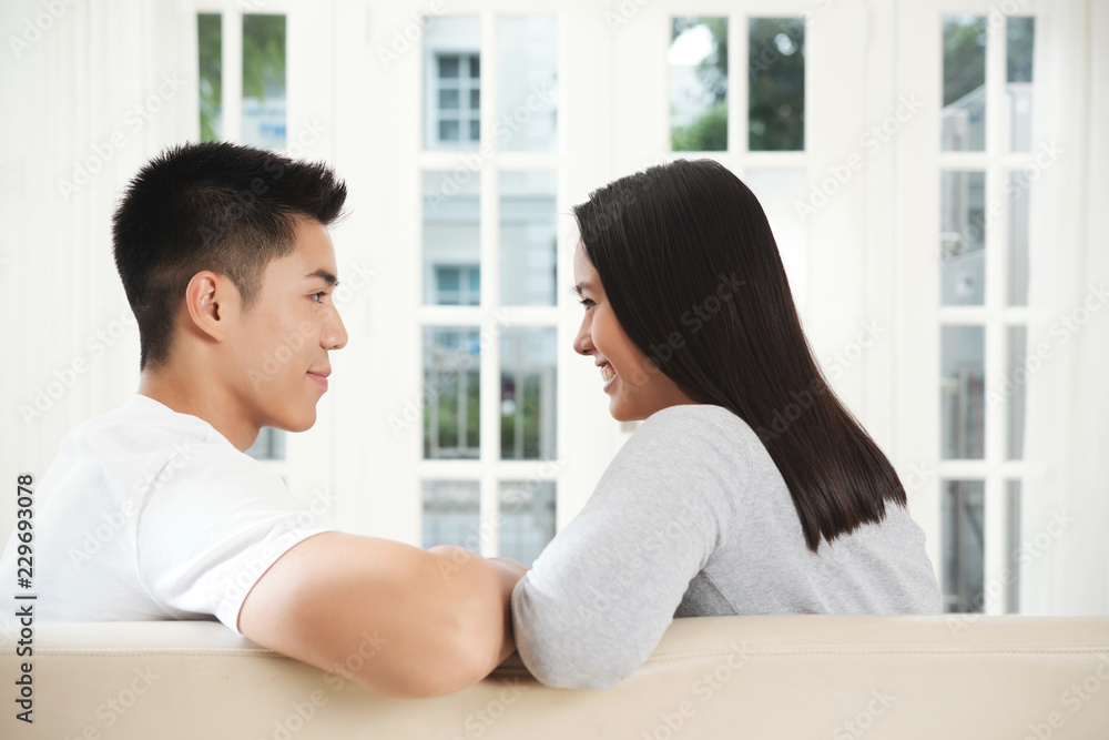 Young couple in love sitting on sofa and chatting, view from the back Young couple in love sitting on sofa and chatting, view from the back