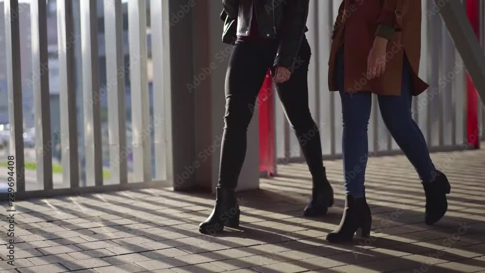 two young slim female friends are going in outdoors in sunny autumn day, close-up of graceful legs