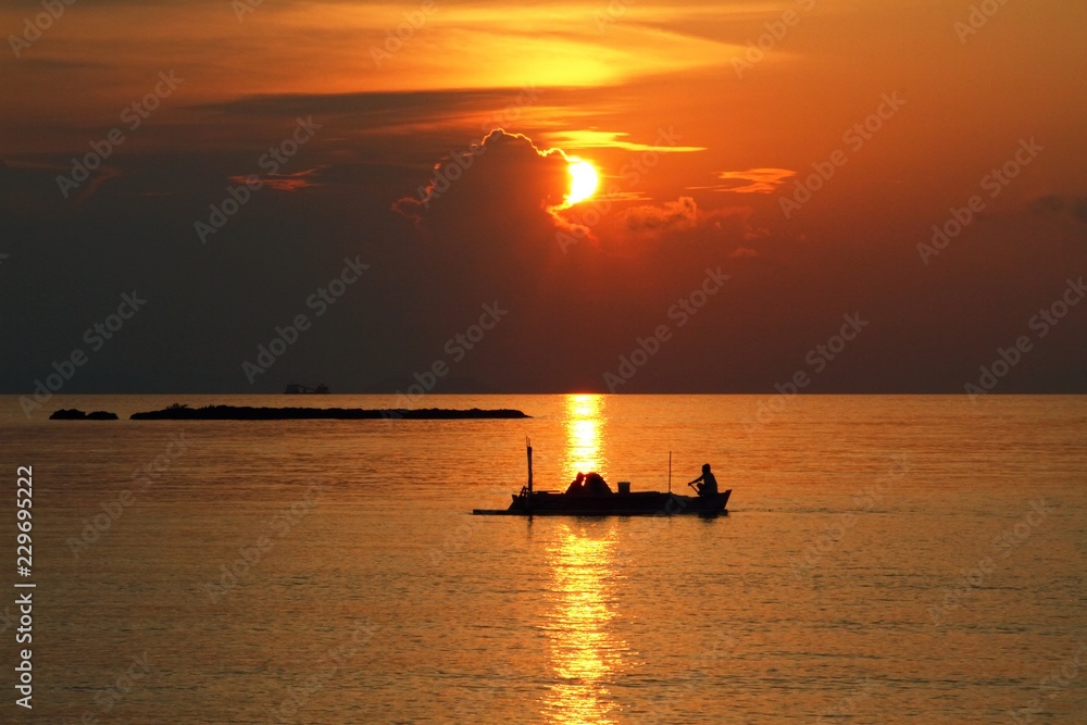 Beautiful sunset with silhouette of fishing boat / Two fishermen sailing home in a traditional wooden boat, Indonesia 