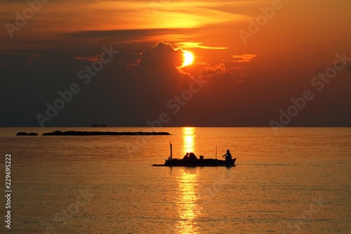 Beautiful sunset with silhouette of fishing boat / Two fishermen sailing home in a traditional wooden boat, Indonesia 