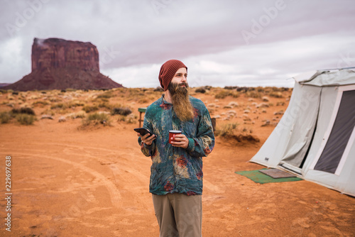 Traveler with mug using smartphone and looking away