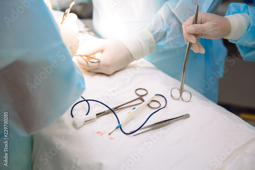 Close-up surgical instruments on a medical table in a clinic during surgery. Metal sterile scissors, clamp, surgical needle at the table or in doctor hand. The concept of health, tools.