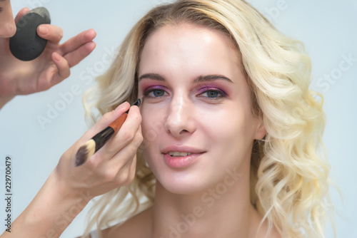 The work of a professional make-up artist, beautician, makes makeup on the face of a blonde girl with shadows on the eyes.