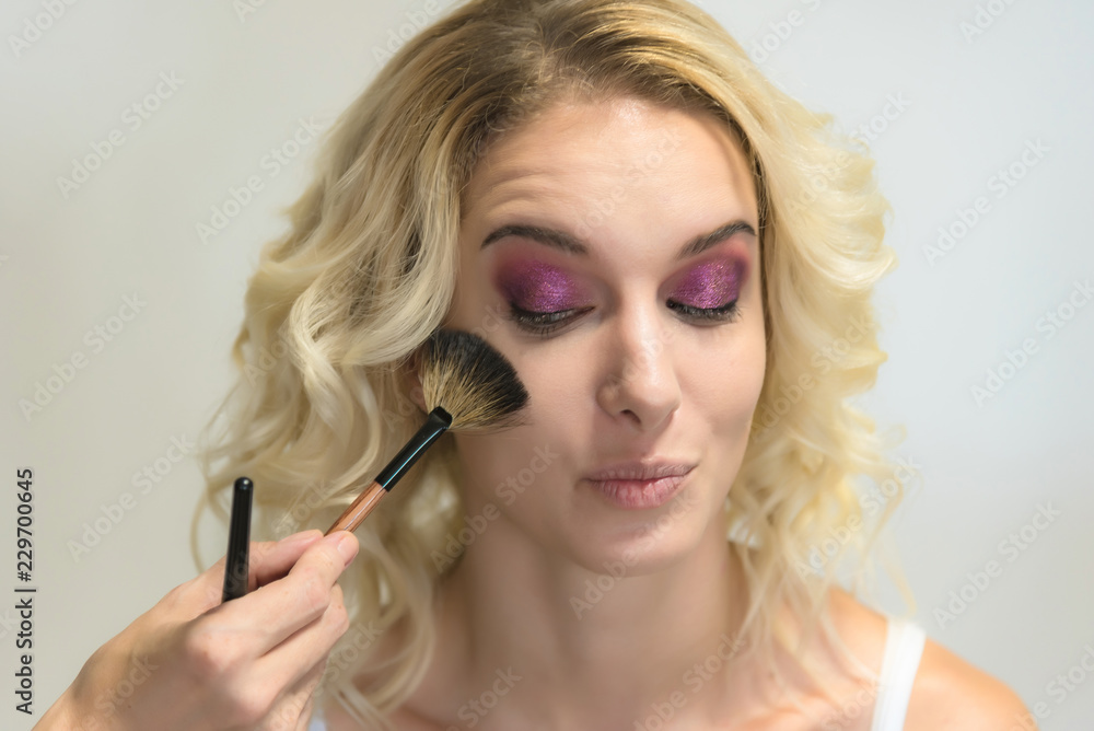 Obraz premium The work of a professional make-up artist, beautician, makes makeup on the face of a blonde girl with shadows on the eyes.
