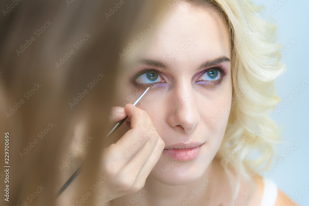 The work of a professional make-up artist, beautician, makes makeup on the face of a blonde girl with shadows on the eyes. The work of a professional make-up artist, beautician, makes makeup on the face of a blonde girl with shadows on the eyes.