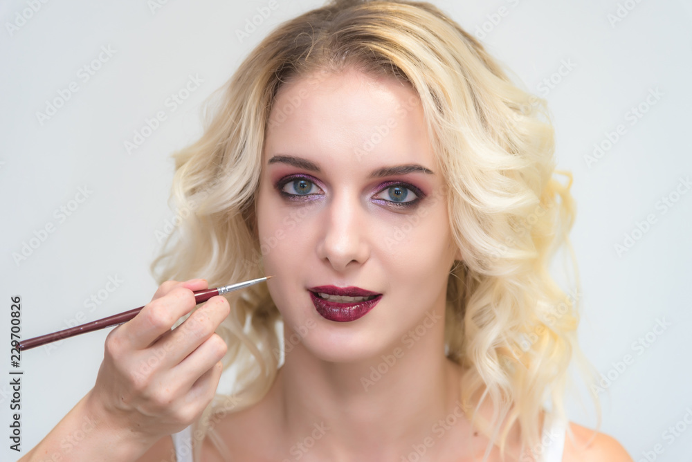 The work of a professional makeup artist - beautician, makes up a brush on the face on the lips of a beautiful blonde. The work of a professional makeup artist - beautician, makes up a brush on the face on the lips of a beautiful blonde.