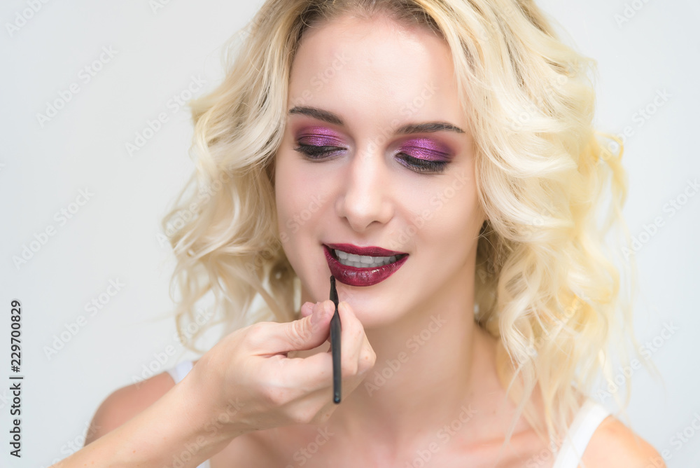 The work of a professional makeup artist - beautician, makes up a brush on the face on the lips of a beautiful blonde. The work of a professional makeup artist - beautician, makes up a brush on the face on the lips of a beautiful blonde.