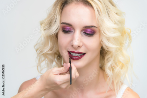 The work of a professional makeup artist - beautician, makes up a brush on the face on the lips of a beautiful blonde.