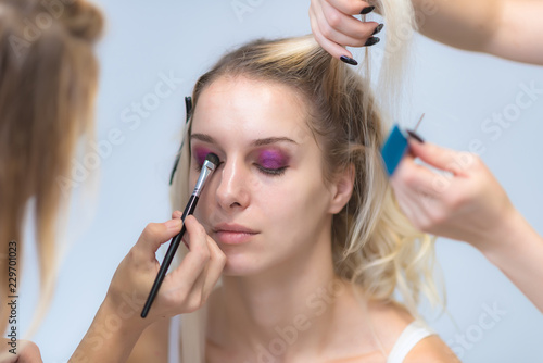 The work of a professional make-up artist, beautician, makes makeup on the face of a blonde girl with shadows on the eyes.