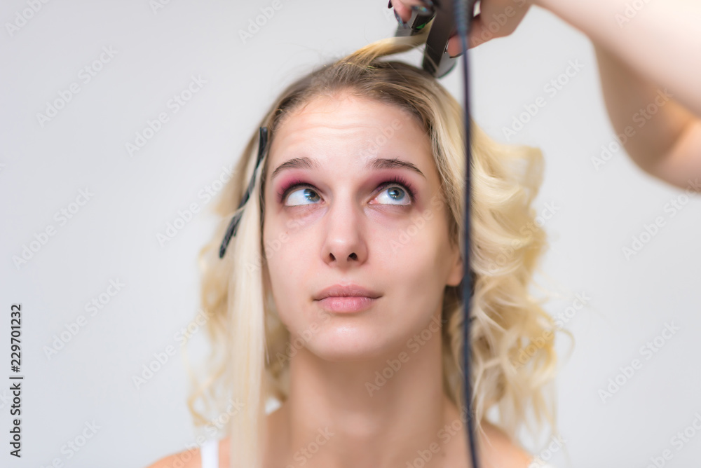 Fototapeta premium The work of a professional makeup artist - hairdresser, makes the hair style of a beautiful blonde girl.