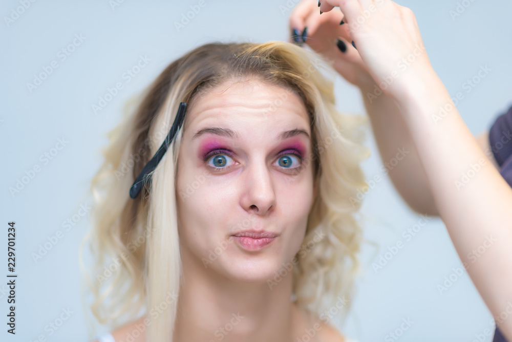 Fototapeta premium The work of a professional makeup artist - hairdresser, makes the hair style of a beautiful blonde girl.