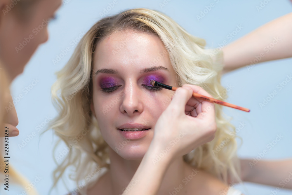 Obraz premium The work of a professional make-up artist, beautician, makes makeup on the face of a blonde girl with shadows on the eyes.