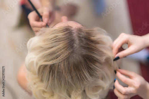 The work of a professional makeup artist - hairdresser, makes the hair style of a beautiful blonde girl.