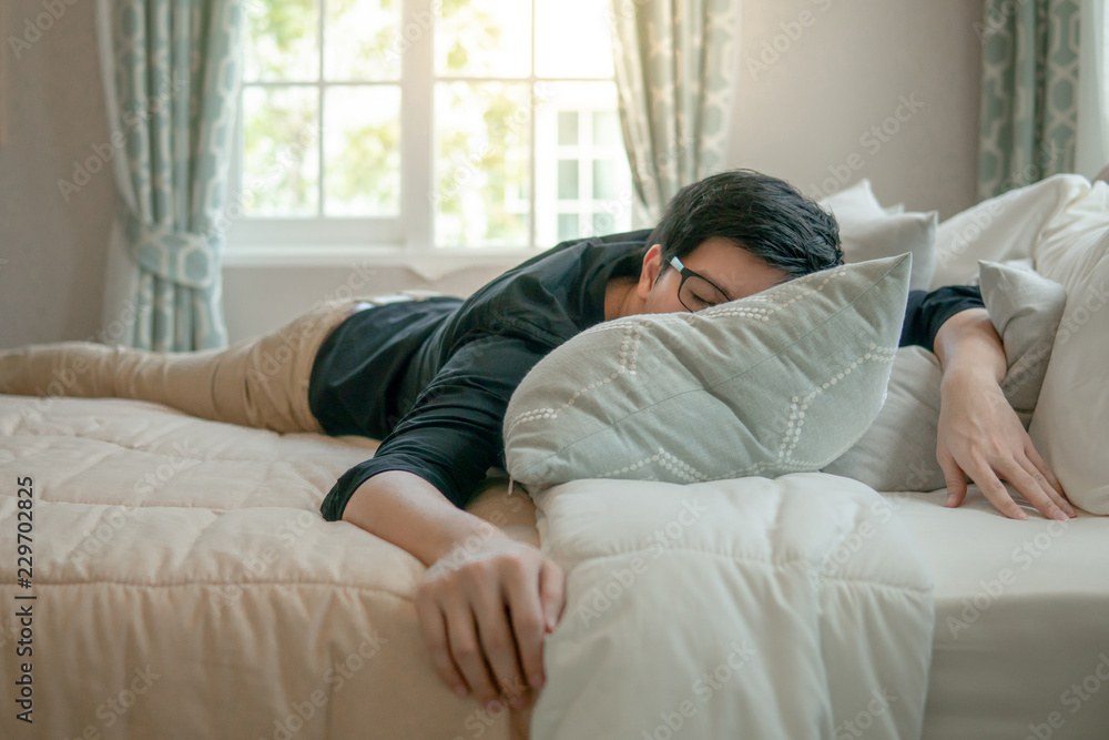 Young Asian man with eyeglasses sleeping on bed in bedroom in the morning. Home living lifestyle concept Young Asian man with eyeglasses sleeping on bed in bedroom in the morning. Home living lifestyle concept
