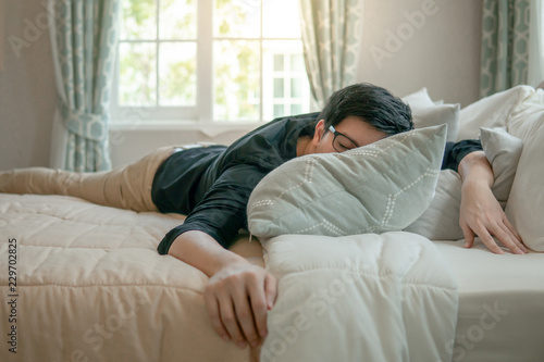 Young Asian man with eyeglasses sleeping on bed in bedroom in the morning. Home living lifestyle concept