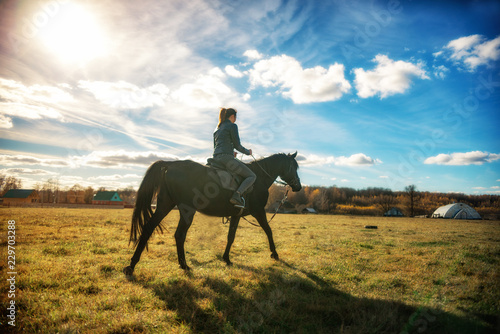 beautiful girl riding a black horse on a Sunny day. equestrian sport