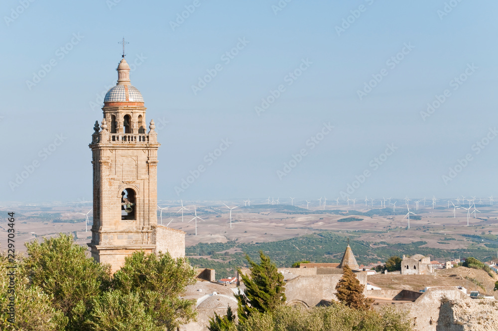 Bell along with ruins of a roofless church, the background is a rural landscape with windmills, is located in the town of Medina Sidonia in Spain. 