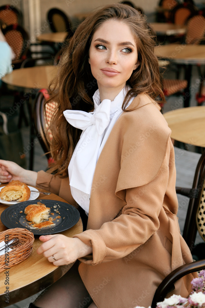 beautiful woman with dark hair in elegant outfit sitting in cafe