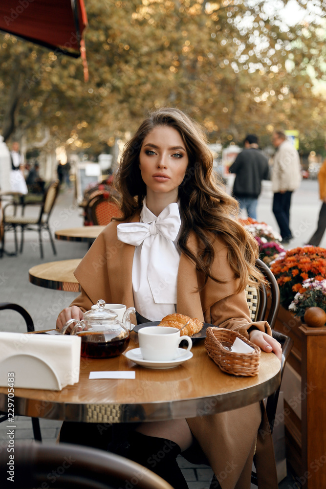 beautiful woman with dark hair in elegant outfit sitting in cafe