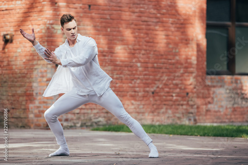 young male ballet dancer in white clothes dancing on urban street