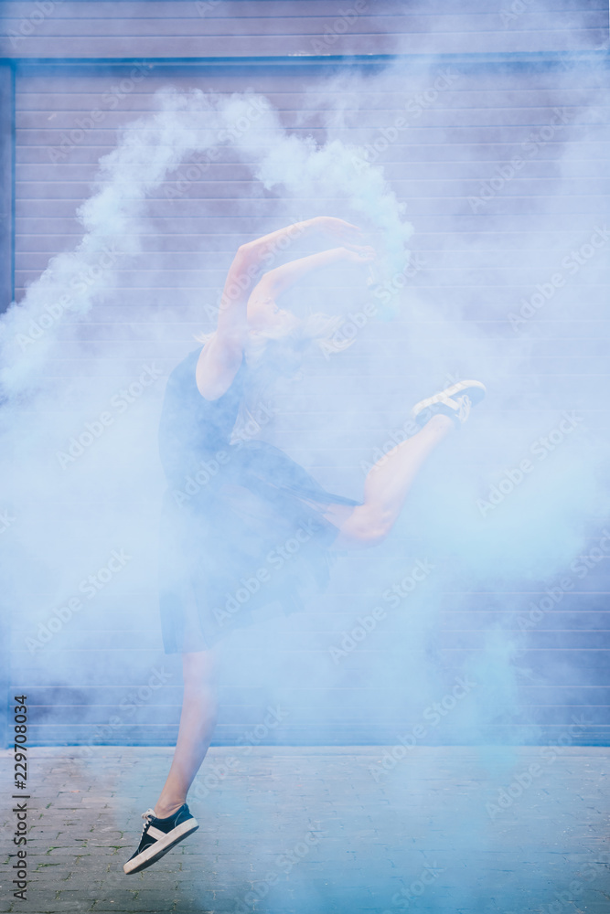 young female contemporary dancer dancing in blue smoke on street young female contemporary dancer dancing in blue smoke on street