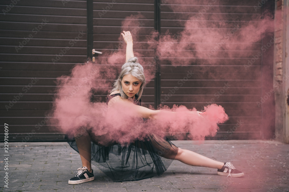 Fototapeta premium piękna dziewczyna tańczy w różowy dym i patrząc na kamery na ulicy