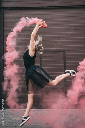 side view of young female dancer dancing in pink smoke on street