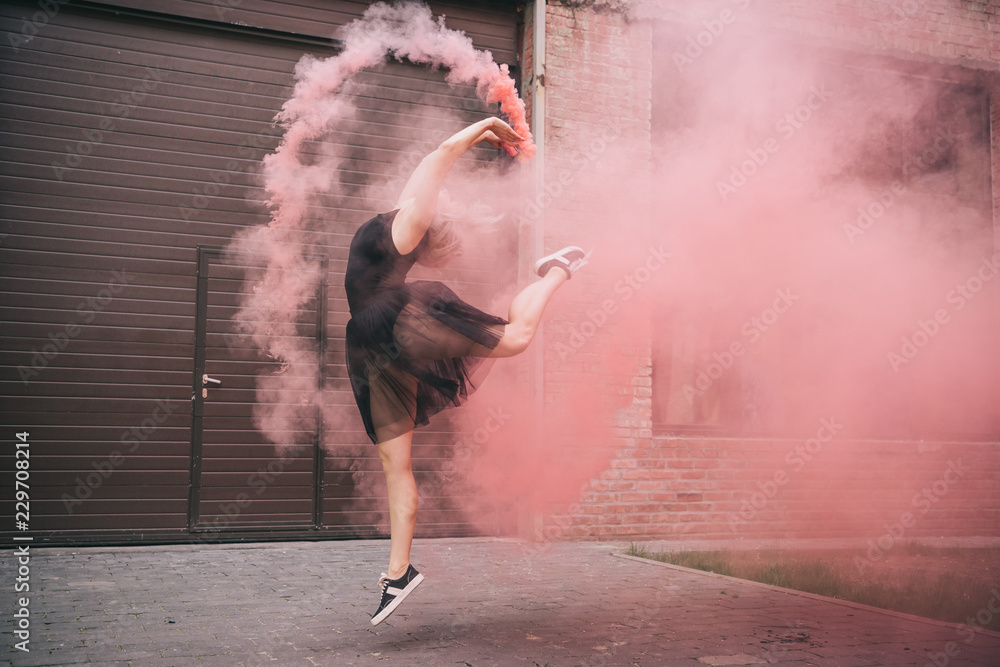 Fototapeta premium atrakcyjna młoda kobieta tańczy w różowy dym na ulicy