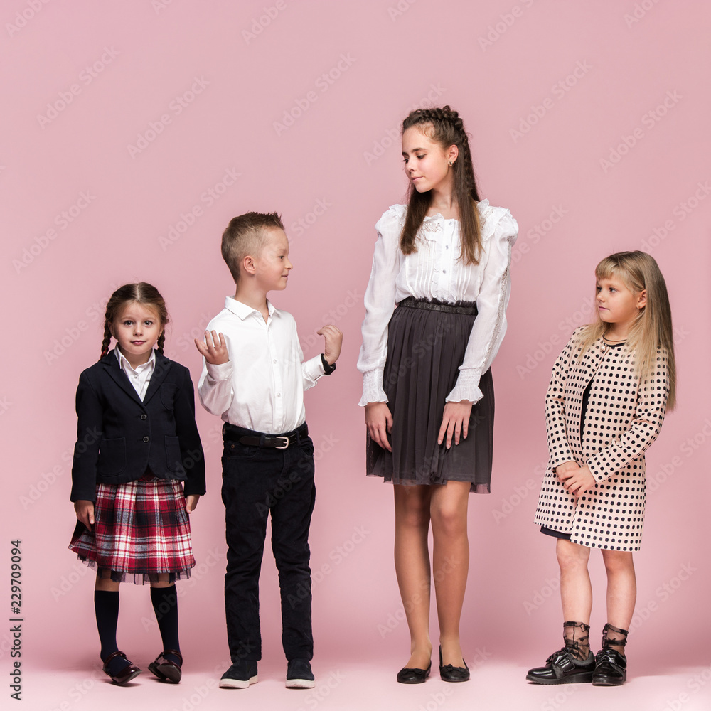 Cute smiling happy stylish children on pink background. Beautiful stylish teen girls and boy standing together and posing at studio. Classic style. Kids fashion and emotions concept. Cute smiling happy stylish children on pink background. Beautiful stylish teen girls and boy standing together and posing at studio. Classic style. Kids fashion and emotions concept.