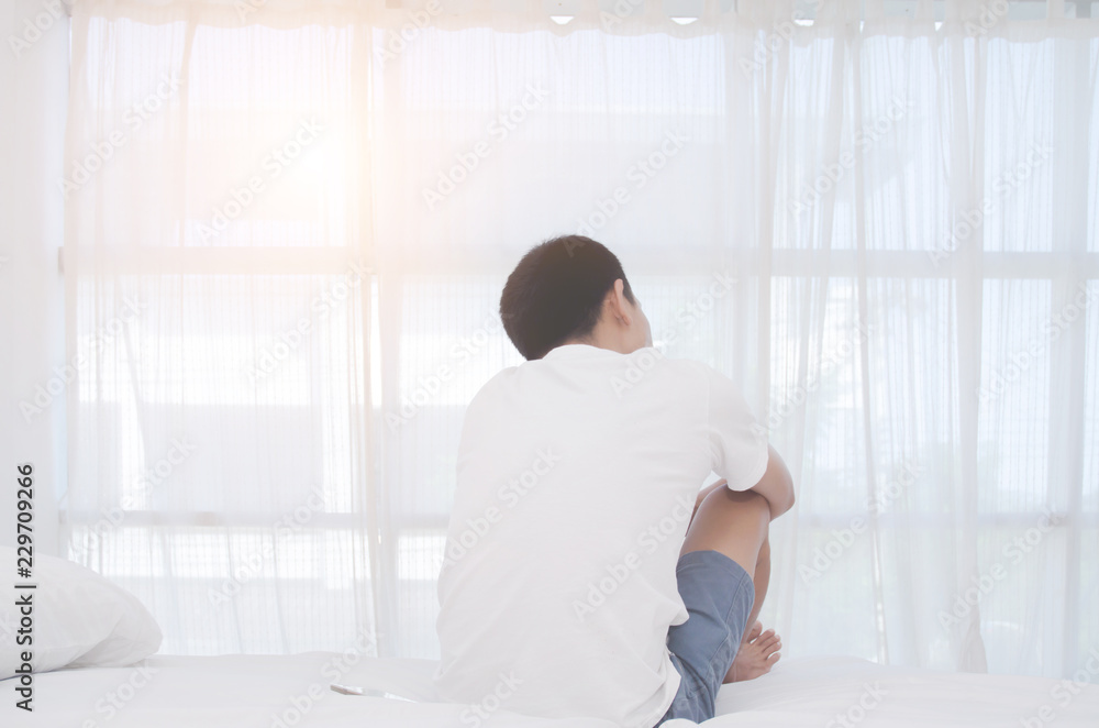 Men are sitting at the edge of the bed in the room and have stress.Young man wearing a white shirt with both hands on his head. Because of pain. Men are sitting at the edge of the bed in the room and have stress.Young man wearing a white shirt with both hands on his head. Because of pain.