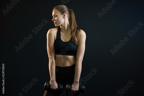 beautiful young girl goes in for sports with dumbbells on a black background