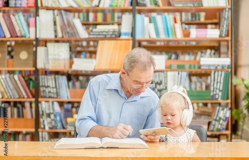 elderly man with a little girl is using a smartphone in the library. Empty space for text